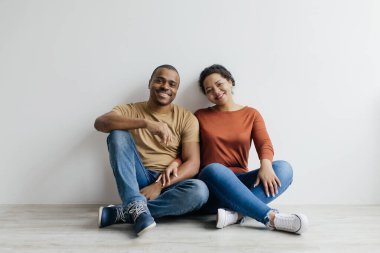 Romantik Afrikalı genç Amerikalı çift beyaz arka planda yerde oturuyor, milenyum siyahi eşlerini seviyorlar, birlikte vakit geçiriyorlar, stüdyoda poz veriyorlar, kameraya bakıp gülümsüyorlar.