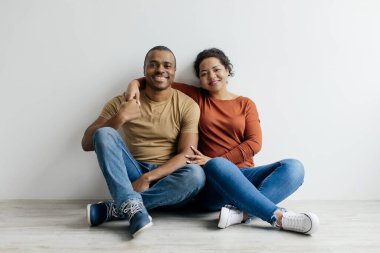 Beyaz arka planda poz veren mutlu, genç siyah bir çiftin portresi. Neşeli, Afro-Amerikan erkek arkadaş ve kız arkadaş yerde oturuyor ve kameraya gülümsüyor.