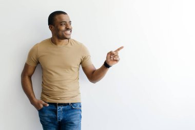 Şuraya bak. Neşeli genç siyahi adam parmak iziyle boşluğu işaret ediyor, beyaz arka planda dururken, Afro-Amerikan erkek reklamlar için bedava yer gösteriyor.