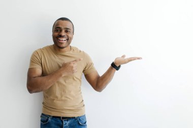 Açık Avuç 'u işaret eden neşeli siyah adam, beyaz arka planda izole edilmiş, Afro-Amerikan erkek reklamcı bir şey tutuyor, görünmeyen nesne tutuyor, kopyalayarak boşluğu dolduruyor.