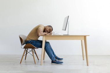 Yorgun Afrikalı Amerikalı bir adam uzun saatler çalıştıktan sonra başını bilgisayarının yanına koyup dinleniyor. Yorgun ve yorgun genç bir siyah erkek masada kestiriyor.