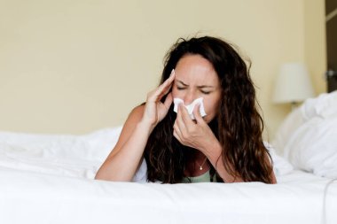 Hasta kadın yatakta uzanıyor, başını tutuyor ve hapşırıyor, genç hasta bir kadın baş ağrısı ya da rahatsızlığı var gibi görünüyor, kıvırcık kadın kendini evde iyi hissetmiyor, grip oluyor, uzay kopyası yapıyor.