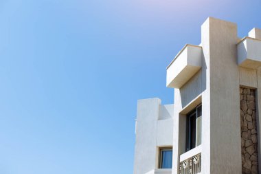 Temiz mavi gökyüzüne karşı taş aksanlı ve geometrik şekilli modern bir bina. Yapı, temiz çizgiler ve minimalist mimari ile çağdaş tasarımı yansıtır, kopyalama alanı