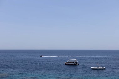 Açık deniz manzaralı, birkaç tekne uzakta seyrediyor. Lüks yatlar suda yüzüyor. Huzuru ve sonsuz ufku yansıtıyor.