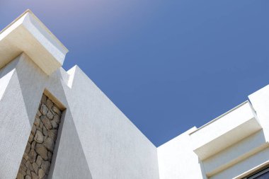 Taş ve beton elementlerle modern bina, geometrik desenler ve parlak mavi bir gökyüzü içeriyor. Mimari tarzı gösterişli ve minimalist, temiz çizgileri vurguluyor, düşük açılı atış.