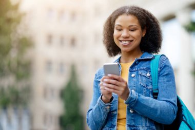 Gülümseyen Afrikalı Amerikalı Kız Öğrenci Şehir Caddesinde Akıllı Telefonla Yürüyor, Mutlu Milenyum Siyahi Kadın Dersten Sonra Eve Giderken Mesajlaşıyor, Boşluğu Kopyala