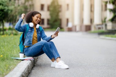 Öyle mi? Neşeli, heyecanlı, genç siyahi bir kadının başarısını dışarıda akıllı telefonla kutlayan, duygusal Afrikalı Amerikalı bir kadının cep telefonu tutuşu ve sıkılmış yumruğu, harika haberler okuması.