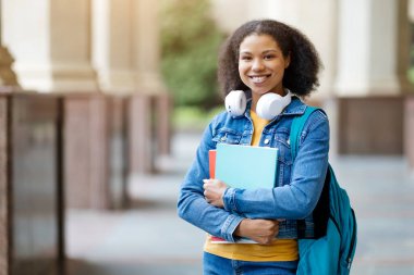 Sırt çantası ve çalışma kitaplarıyla üniversite kampüsünde poz veren Afro-Amerikan bayan öğrenci, kameraya bakan mutlu siyahi kadın, öğrenci yaşam tarzından zevk alan, kopyalama alanı