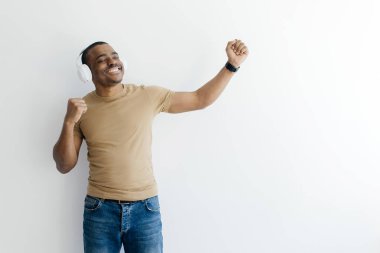 Pozitif genç adam müzik dinlemekten, dans etmekten ve eğlenmekten zevk alıyor. Bin yıllık neşeli Afrikalı Amerikalı adam beyaz stüdyo arka planında kablosuz kulaklık takıyor.