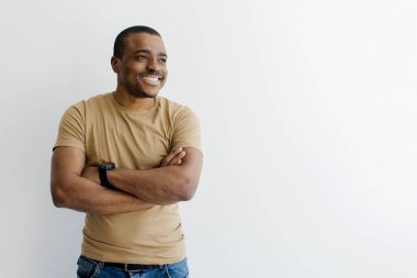 Yakışıklı genç siyah adam kollarını kavuşturmuş ve fotokopi alanına bakıyor, gülümseyen Afrikalı Amerikalı erkek iyi bir şey düşünüyor, beyaz arka planda poz veriyor.