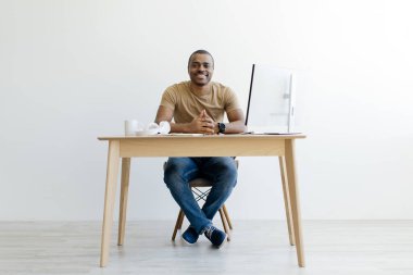 Yakışıklı genç siyahi adam evinde bilgisayarla oturmuş kameraya gülümsüyor, Afrikalı Amerikalı serbest çalışan, uzaktan kumandalı iş fırsatlarının tadını çıkaran, boşluğu kopyalayan...