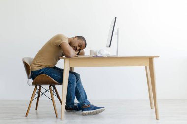 Afrika kökenli Amerikalı bir adam bilgisayar monitörünün önünde uyuyor, yorgun siyah bir adam modern bir stüdyo ortamında mola veriyor, iş yerinde yorgunluk hissediyor, yan görüş