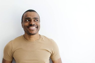Bej tişörtlü gülümseyen Afro-Amerikan adam, düşünceli bir ifadeyle yukarı bakıyor, beyaz stüdyo arka planında duran meraklı siyah erkek, bir şeyin hayalini kuruyor, boşluğu kopyalıyor