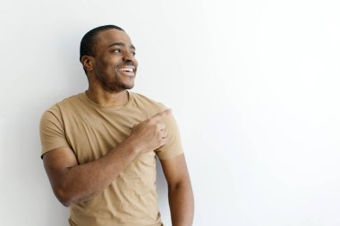 Şuraya bak. Kopya uzayı işaret eden neşeli, Afro-Amerikalı genç adam, Stüdyoda beyaz arka plan üzerinde poz veren, el yazısı için boş alan gösteren mutlu siyah adam.