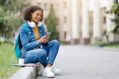 Gülümseyen Siyah Kız Öğrenci Akıllı Telefonla Üniversite Binası 'nın yanında rahatlıyor, Arkadaşlarıyla Mesajlaşan Afro-Amerikan Kadın İnternette veya Yeni Uygulama Bakıyor, Boşluğu Kopyala