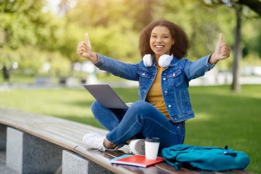 Siyahi Öğrenci Kadın Laptopuyla poz veriyor ve parmaklarını havaya kaldırıyor, Afro-Amerikan kadın gülümsüyor Yeşil Park 'ta oturuyor, Çevrimiçi Eğitimi Onaylıyor