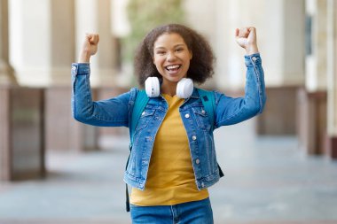 Başarılı bir öğrenci. Neşeli Siyah Kadın Kollarını Yükseltiyor ve Açık havada Başarıyı Kutluyor, Heyecanla Yumruk Sallıyor, Sırt çantasıyla Dışarıdaki Üniversiteye Yakın Poz Veriyor, Boş Alan