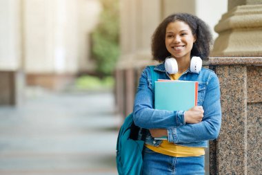 Üniversite kampüsündeki mermer bir sütunun yanında duran siyah öğrenci kadın, Afro-Amerikan kadın kendine güvenerek gülümsüyor ve yana bakıyor, boşluğu kopyalıyor.