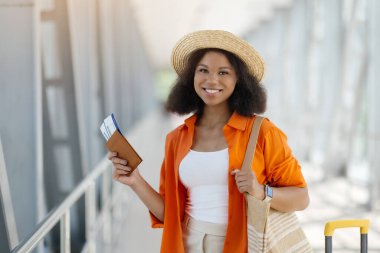 Havalimanı terminalinde saman şapkalı güzel siyahi bir kadının portresi, mutlu gülümseyen Afrikalı bir Amerikalı kadının tatil için hazır olması, pasaport ve biniş kartı tutması, kopyalama alanı.