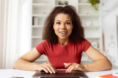 Heyecanlı, genç, siyah bir kadının evdeki bilgisayarını kullanması, neşeli, Afrikalı, Amerikalı, serbest çalışan bir kadının ekrana bakması ve klavyede yazı yazması, online teklif sunması, webcam bakış açısına tepki vermesi.