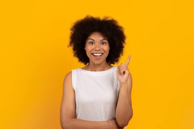 Fikir kavramı. Heyecanlı kıvırcık saçlı genç Afrikalı Amerikalı kadın şaşırmış bir ifadeyle parmağını kaldırıyor, neşeli siyah kadın sarı stüdyo arka planında duruyor, boşluğu kopyalıyor.