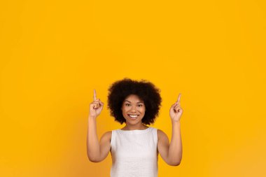 Harika bir teklif. Kafasının üstündeki fotokopi çekilen boşluğu işaret eden heyecanlı Afrikalı Amerikalı kadın, sarı stüdyo arka planının üzerinde sizin için bedava bir yer olduğunu gösteren mutlu siyah kadın.