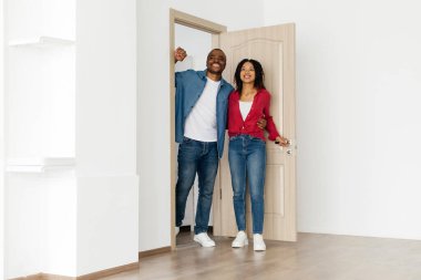 Neşeli siyah çift yeni dairenin kapısında duruyor, kendinden emin bir şekilde gülümsüyor, genç mutlu Afrikalı Amerikalı eşler modern temiz uzayda yolculuklarına başlıyorlar,