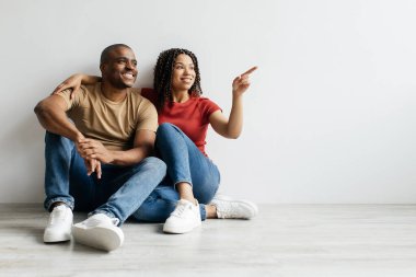 Beyaz Duvar 'ın yanında oturan, gülümseyen, Afro-Amerikalı genç çiftin tasarım ve reklamın için kopyalama alanı gösteren mutlu siyah milenyum eşleri,