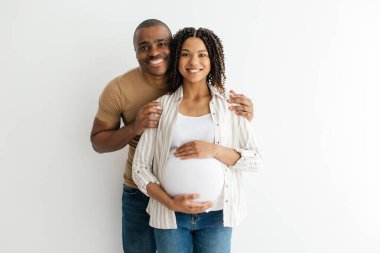 Hamile siyahi çift, evde duvarın yanında beklerken, bebek, kadın ve erkeğin kameraya gülümseyip Uzay 'ı kopyaladığı mutlu genç eşlerin portresi