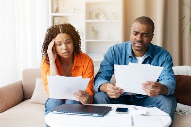 Faturaları kontrol eden, kanepede oturan, kredi belgelerini okuyan, elinde gazete tutan, aylık harcamaları sayan, aile bütçesini planlayan mutsuz Afrikalı erkek ve kadın.