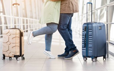 Havalimanında kucaklaşan genç siyahi çift, bavulları yanında, duygusal veda ya da birleşme anı, günlük kıyafetleri ve modern bavulları ile tüm vücut görünümü, kırpılmış çekim