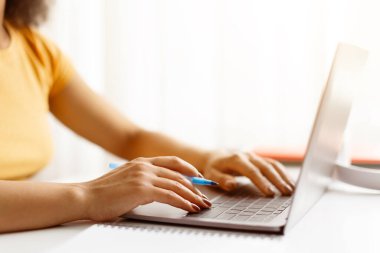 Dizüstü bilgisayarda elinde kalemle yazı yazan ellerin yakın çekimi. Ev ofis çalışma alanından uzak çalışma veya çevrimiçi öğrenme ayrıntıları sahnesi, kırpılmış görüntü