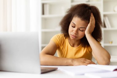 Yorgun, genç siyahi bir kadın, evde otururken gözleri kapalı, elini uzatmış dinleniyor. Uykulu ya da zihinsel olarak çevrimiçi çalışmadan ya da uzaktan çalışmadan tükenmiş, yakın plan