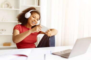 Kırmızı tişörtlü neşeli genç siyahi kadın işten izin alıp gezici oyun oynuyor ya da evde ders çalışıyor. Uzak rutin sırasında rahatlama ve dijital yaşam biçimi, kopyalama alanı