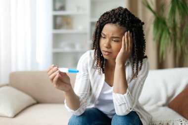 Siyahi bir kadın endişe ve şaşkınlıkla hamilelik testine bakıyor. Duygusal yansıma, sağlık farkındalığı ve hayatı değiştiren olasılıklar, yakın çekim.