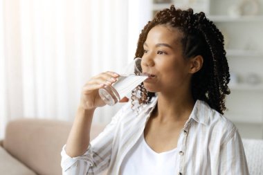 Genç hamile bir kadın evinde kanepede su içiyor ve hamileliği boyunca susuz kalmıyor. Sakin ve sağlıklı bir yaşam tarzı, doğal ışık ve yumuşak tonlarda, samimi bir ortam, yakın çekim.