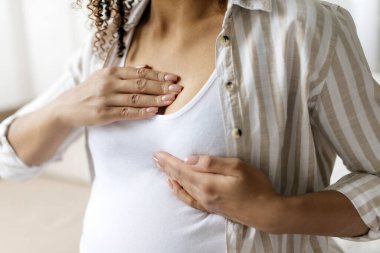 Göğsünü tutan siyah hamile bir kadın, göğüs hassasiyetini gösteriyor. Hamilelik süresince hormonal değişimlerin ve vücut hassasiyetinin gerçek belirtilerini gösterir.
