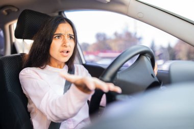 Kızgın Hintli kadın sürücü arabanın içinde saldırgan bir şekilde el kol hareketi yapıyor. Yol öfkesi, hüsran veya trafik tartışması kavramı, gerçek duygu ve kentsel sürüş yoğunluğunu yakalamak
