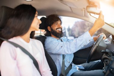 Kadın bakarken gülümseyen Hintli adam dikiz aynasını ayarlıyor. Güvenli sürüş alışkanlıklarını, günlük konuşmaları ve bir yolculukta ilişki uyumunu gösterir, yakın plan.