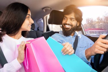 Alışveriş torbalarıyla arabada otururken Hintli çift birbirlerine gülümsüyor. Aşk, neşe, bağ, ilişki mutluluğu ve paylaşılan yaşam tarzını temsil eder..