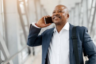 Havaalanında cep telefonuyla konuşan siyahi iş adamının yakın plan portresi, iş seyahatleri sırasında Afro-Amerikan erkek telefon konuşmasının keyfini çıkarıyor