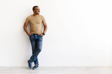 Rahat Afro-Amerikan bir adam beyaz duvara yaslanmış ve fotokopi odasına bakıyor. Mutlu genç yetişkin gülümsemesi ve rahat modern mekanda gündelik yaşam tarzının tadını çıkarıyor.