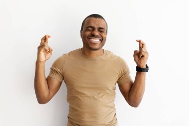 Afro-Amerikan bir adam iki elini de çapraz yapıp umutla gülümsüyor. İyi şans, hüsnükuruntu ya da iyimserliği oyuncu ve sıradan stüdyo çekimleriyle ifade etmek, boşluğu kopyalamak