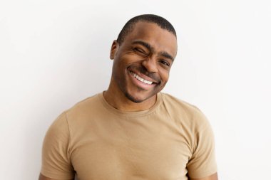 Neşeli bir adamın neşe içinde göz kırpan ve gülümseyen portresi. Beyaz arkaplanda hafif gündelik stüdyo ortamında çekici ve esprili yüz, kopyalama alanı