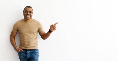 Tişörtlü gülümseyen adam fotokopi alanını eliyle işaret ediyor. Temiz beyaz arka plan, panorama, ürün ya da yön öneren dostane ve kendinden emin bir jest