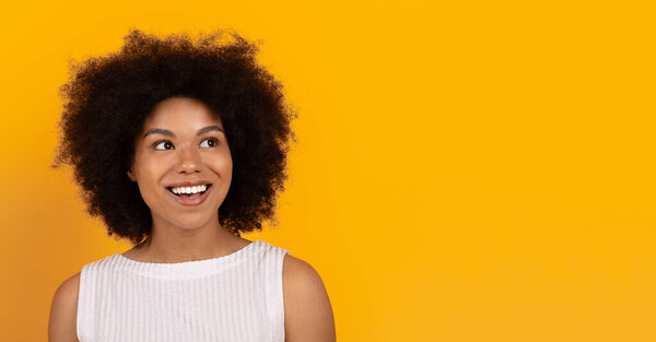 Happy young African American woman smiling and looking aside at copy space on yellow studio background. Positive emotion, stylish expression and joy, panorama
