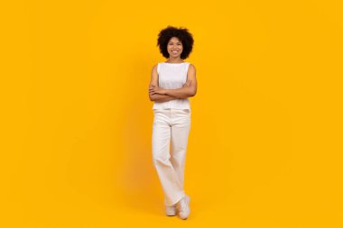Sarı stüdyo arka planında kollarını kavuşturmuş, kendinden emin, Afro-Amerikan bir kadın. Kendine güvenen ve modern titreşimli sıradan moda portresi, kopyalama alanı