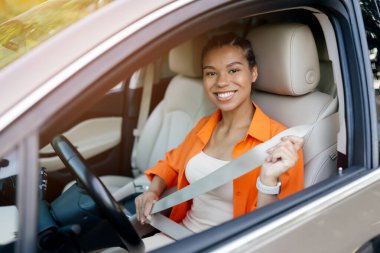 Şoför koltuğunda emniyet kemerini bağlarken gülümseyen genç siyahi kadın. Güvenlik, sorumluluk ve pozitiflik modern bir sürüş bağlamında, yakın çekim