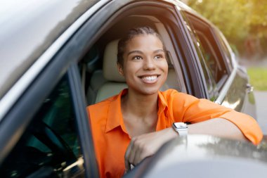 Araba camından dışarı bakarken gülümseyen güzel siyah bir kadın. Yansıtıcı ve umut dolu bir an, temiz havanın ve manzaranın tadını çıkarıyor, yakın plan.