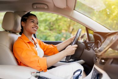 Genç siyahi kadın kendine güvenen bir gülümsemeyle araba sürüyor. Pencereden gün ışığı akışı, yenilenmiş odak, enerji ve yeni bir zihniyet, yakın çekim önerisi